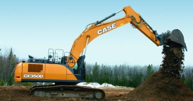 An orange Case excavator sitting on dirt at a construction site with an overcast sky background and trees in the background.