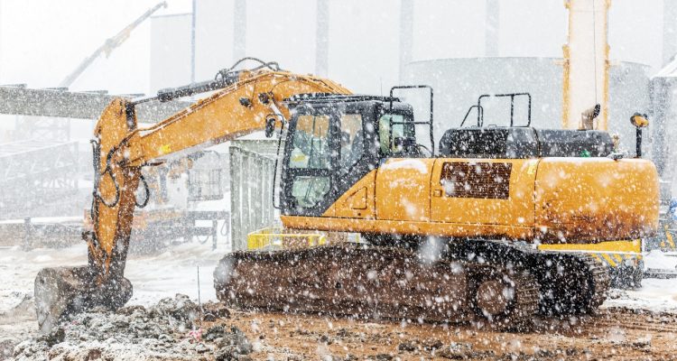 A power tan wheel loader working at a winter construction site in the cold weather with light snow falling.
