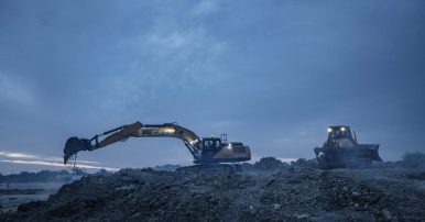 A CASE backhoe and bulldozer operating on a construction site after sunset with a cloudy sky background and low light.