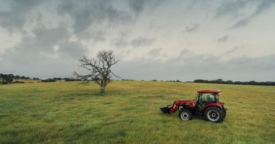 A bright red Case IH machine driving through a wide open grass field in Texas with an overcast sky.