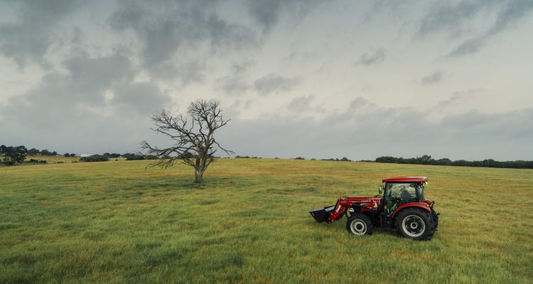 A bright red Case IH machine driving through a wide open grass field in Texas with an overcast sky.