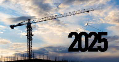 Silhouette of a construction crane against a blue cloudy sky, raising the number 2025 into the air.