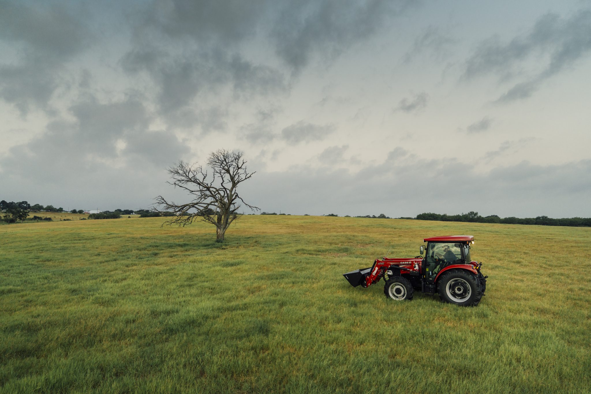 A bright red Case IH machine driving through a wide open grass field in Texas with an overcast sky.