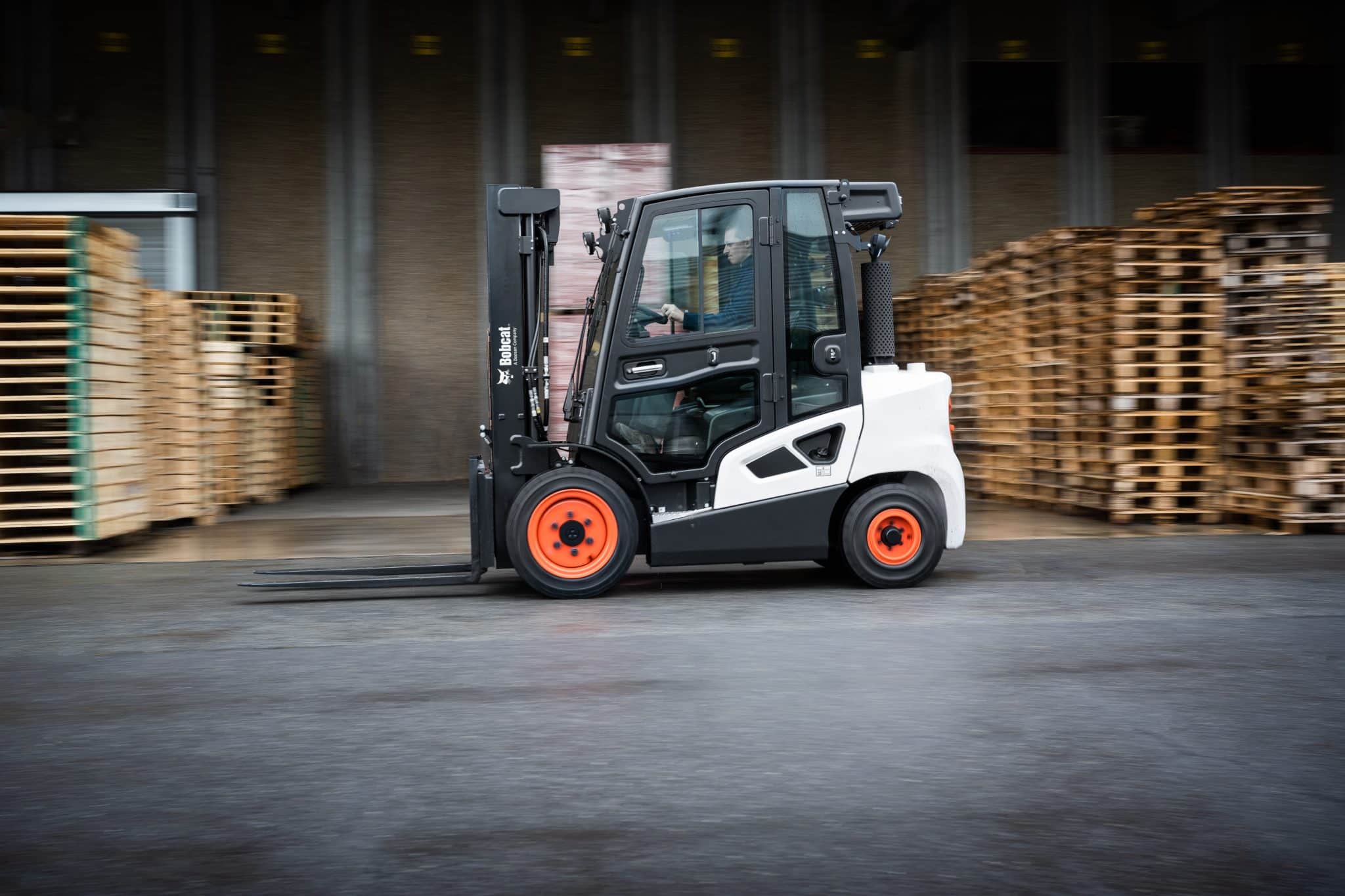 A black and white Bobcat Forklift moving pallets in an industrial warehouse setting.